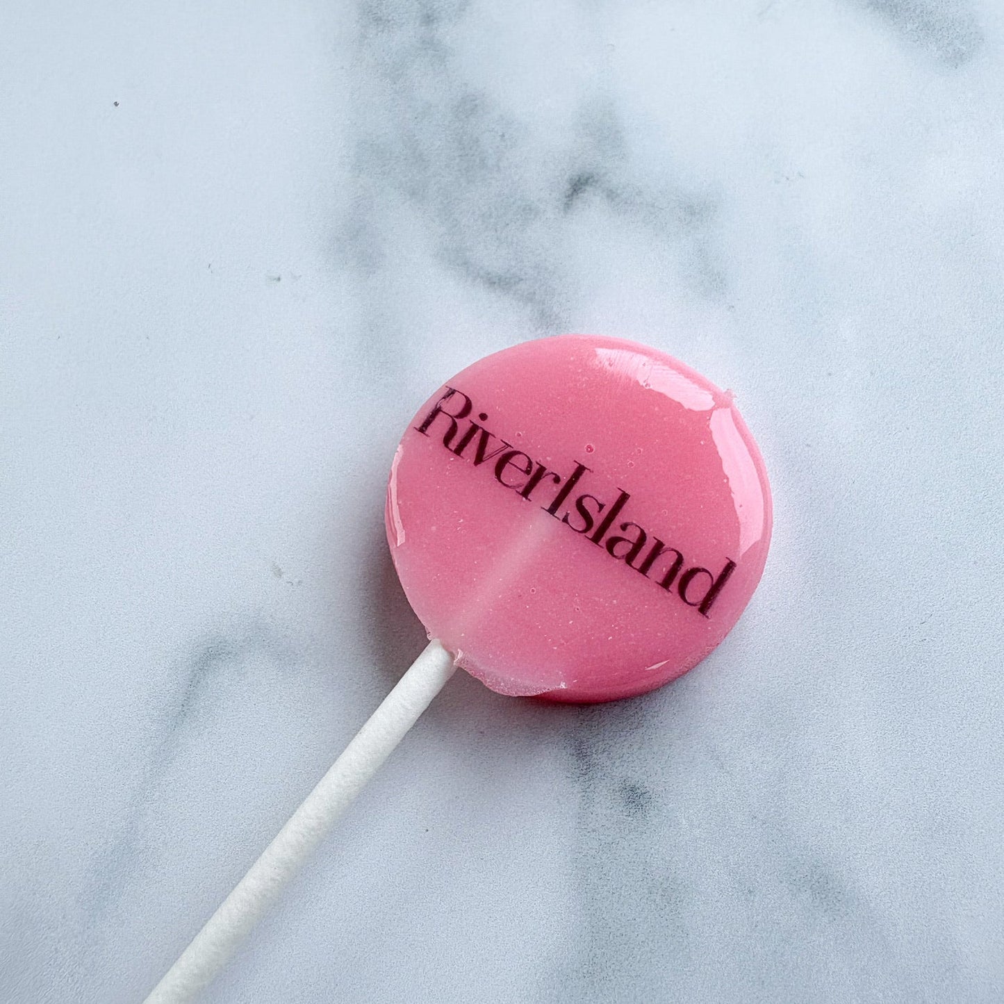Pink lollipop with 'RiverIsland' branding on a marble background