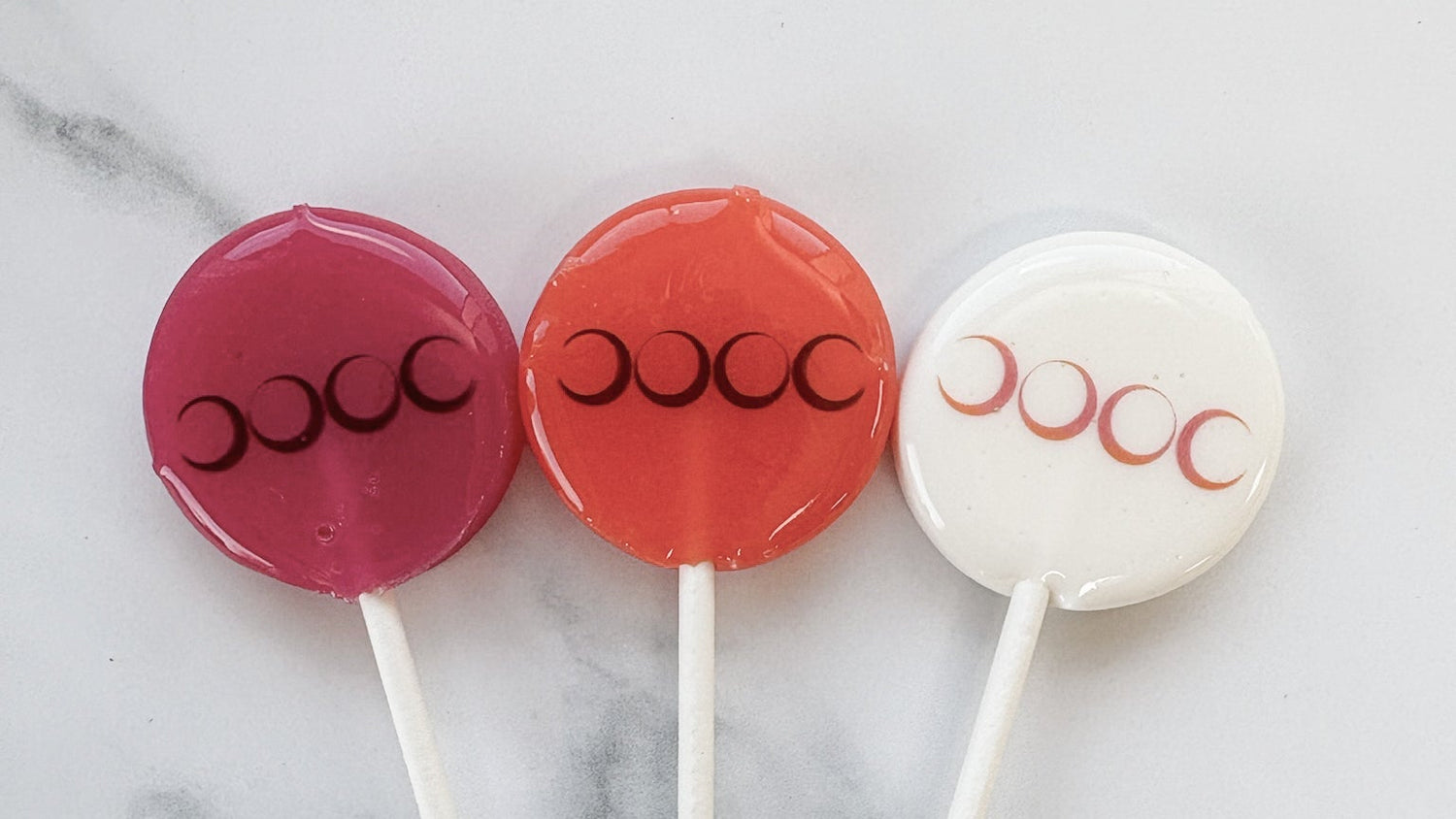 Three lollipops with branding on a marble surface