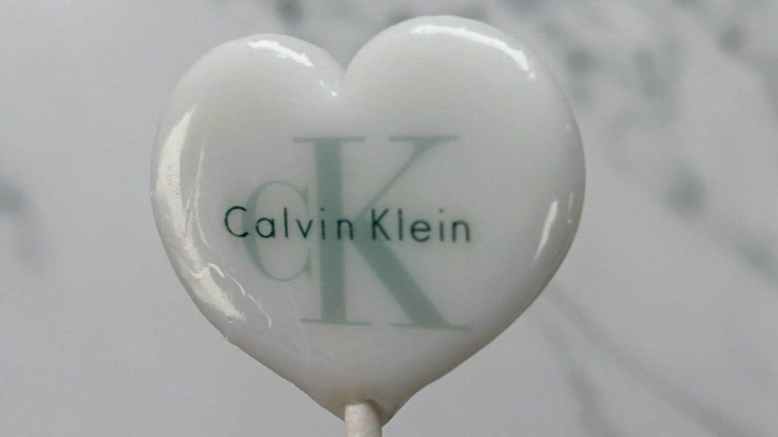 Heart-shaped lollipop with Calvin Klein logo on a marble background