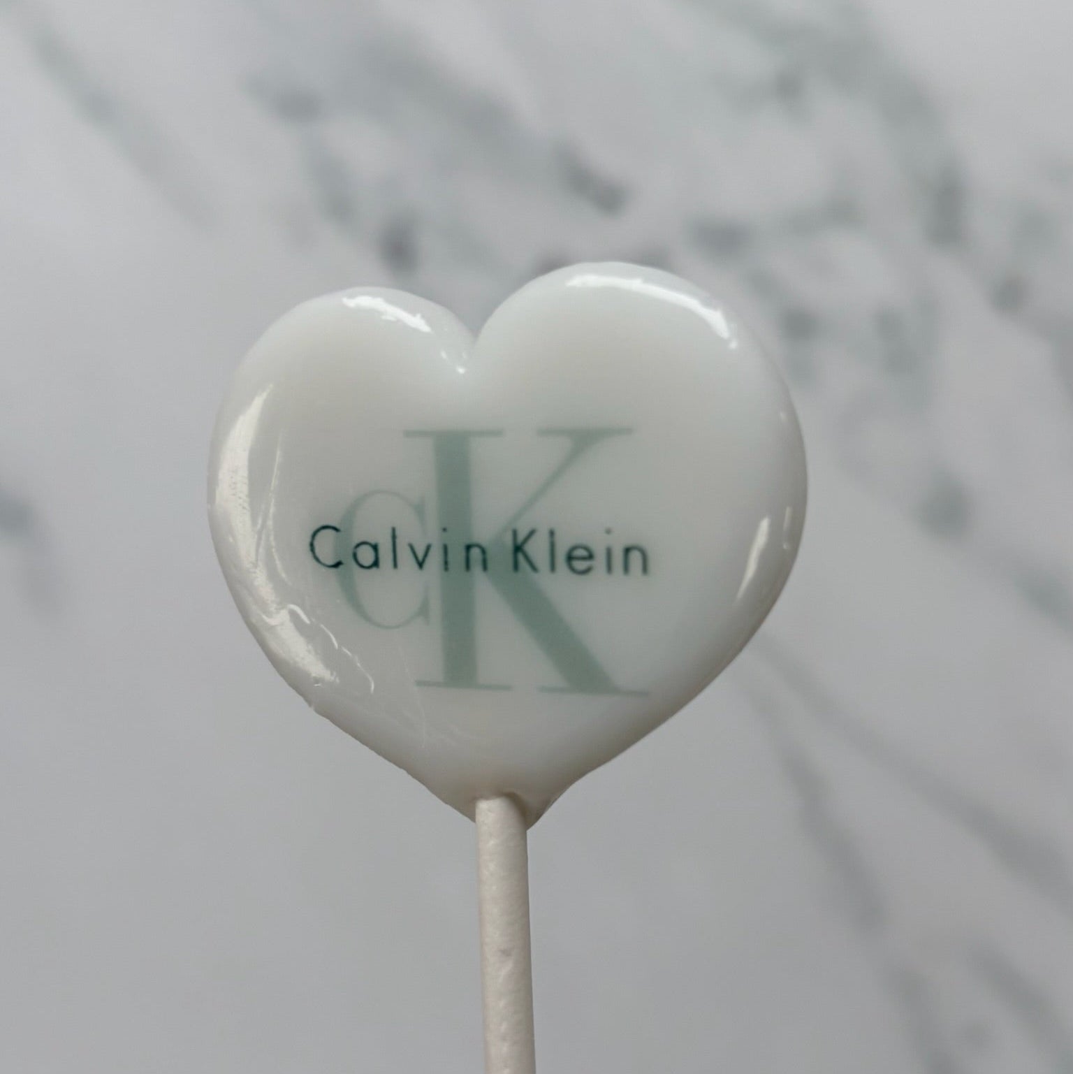 Heart-shaped lollipop with Calvin Klein logo on a marble background
