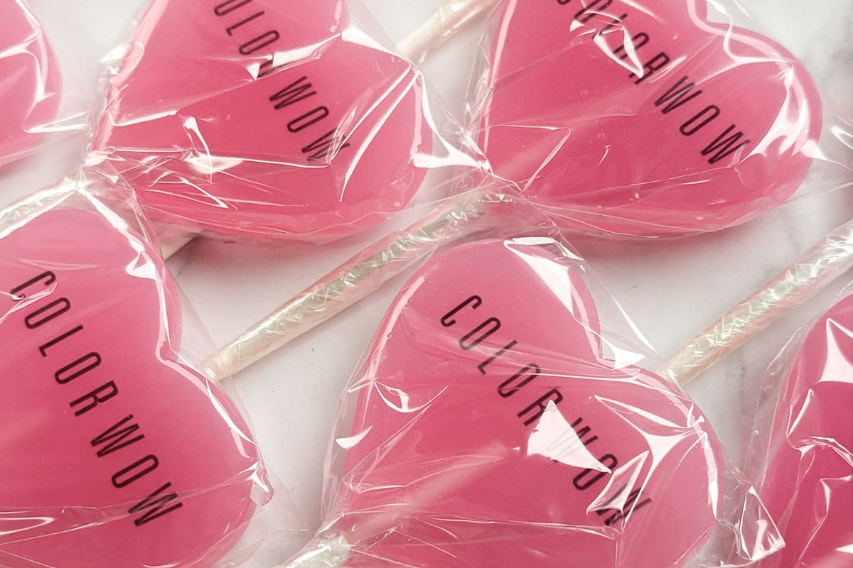 Pink heart-shaped lollipops with 'Color Wow' branding on a marble surface.