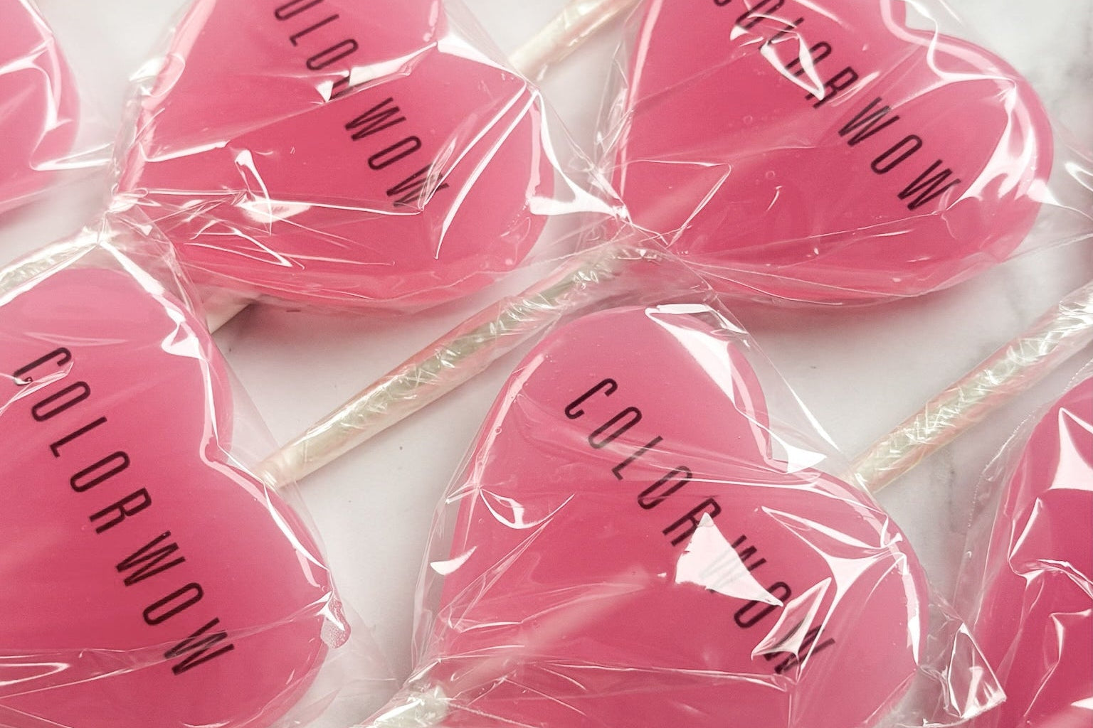 Pink heart-shaped lollipops with 'Color Wow' branding on a marble surface.
