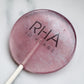 Pink lollipop with 'RHA' branding on a marble surface