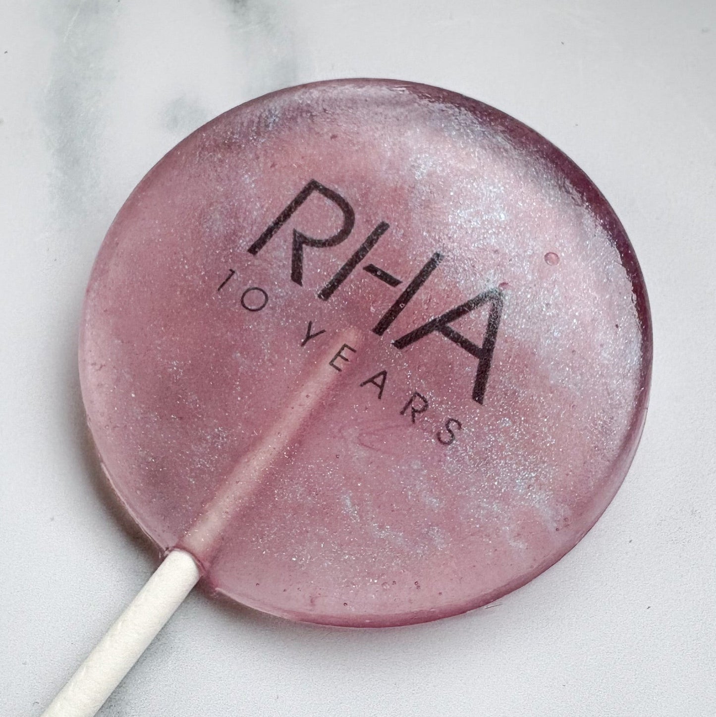Pink lollipop with 'RHA' branding on a marble surface