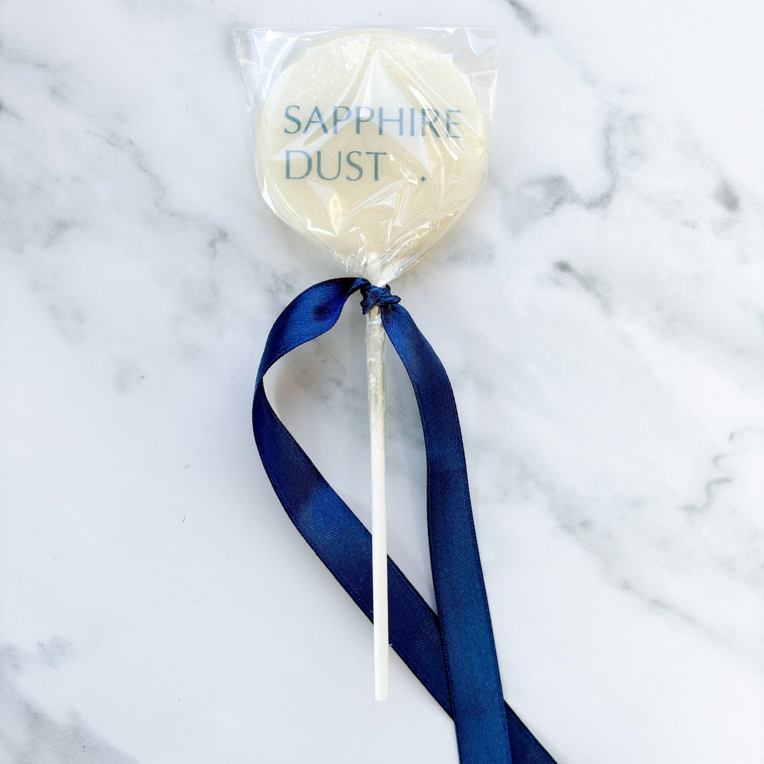 Sapphire Dust lollipop with a blue ribbon on a marble background