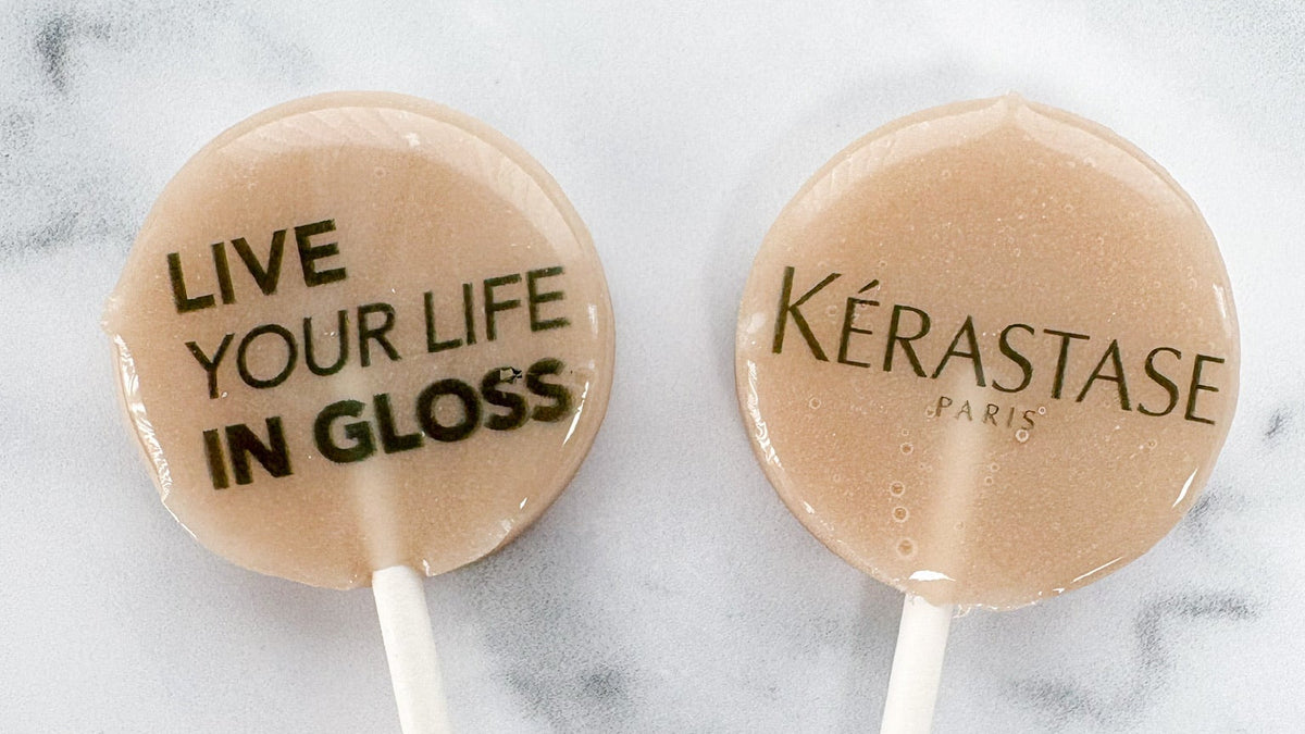 Two lollipops with 'Kérastase Paris' and 'Live Your Life in Gloss' text on a marble background.
