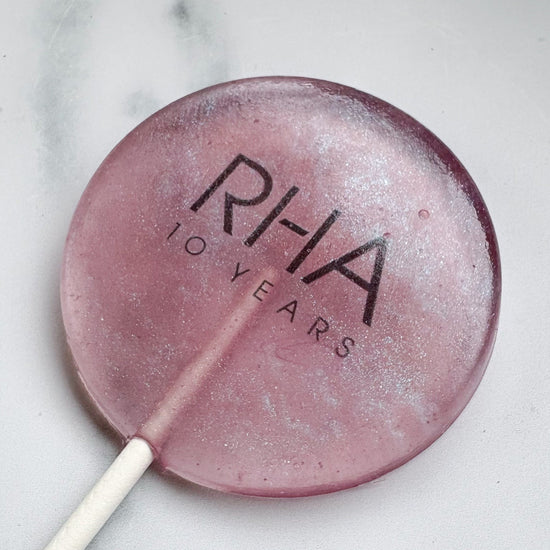 Purple Iridescent lollipop with 'RHA' branding on a marble surface